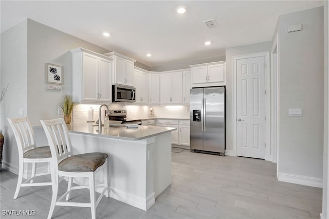 kitchen featuring a kitchen bar, appliances with stainless steel finishes, white cabinetry, kitchen peninsula, and tasteful backsplash