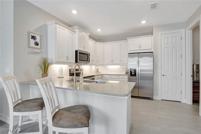 kitchen with appliances with stainless steel finishes, backsplash, sink, white cabinetry, and a kitchen bar