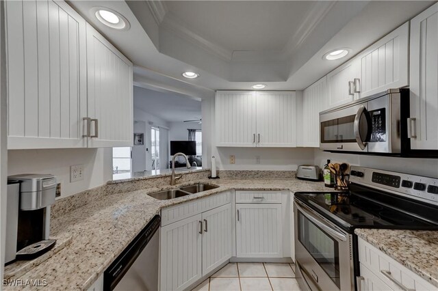 kitchen featuring appliances with stainless steel finishes, ornamental molding, a tray ceiling, white cabinetry, and a sink