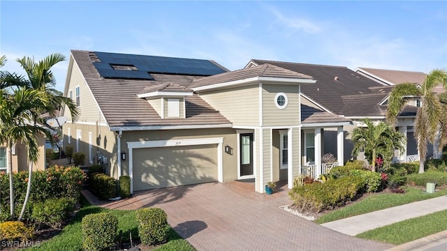 view of front facade featuring a garage, solar panels, decorative driveway, and a tiled roof