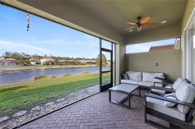 sunroom with a ceiling fan, a residential view, and a water view