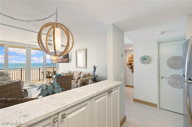 180 Seaview Ct Unit 911, Marco Island, FL 34145 - kitchen with open floor plan, light stone countertops, a water view, baseboards, and white cabinets