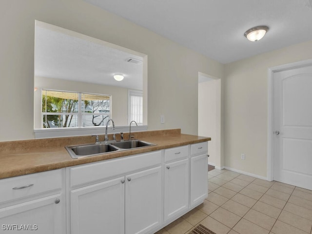 kitchen with visible vents, white cabinets, a sink, light tile patterned flooring, and baseboards