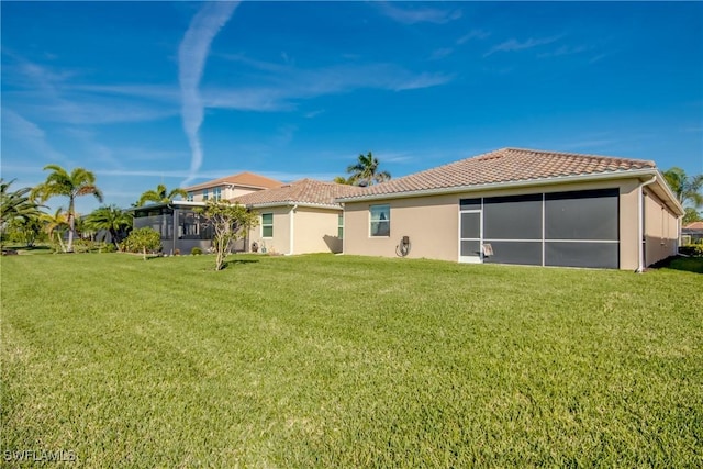 back of house featuring a sunroom, a tile roof, a lawn, and stucco siding