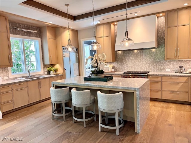 kitchen with a kitchen bar, sink, a tray ceiling, a kitchen island, and light brown cabinetry