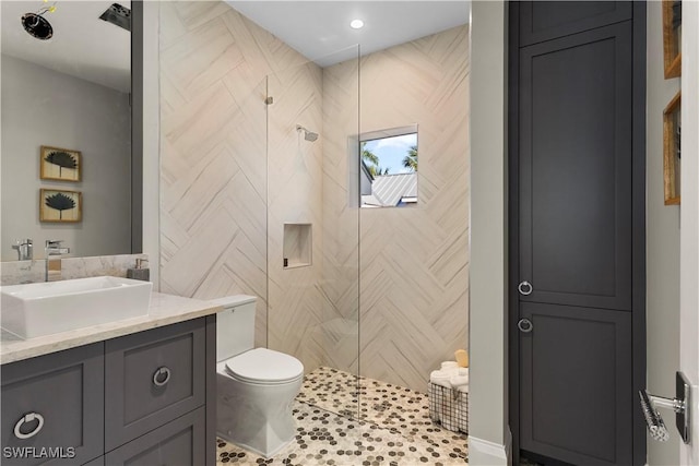 bathroom with a tile shower, toilet, vanity, and tile walls