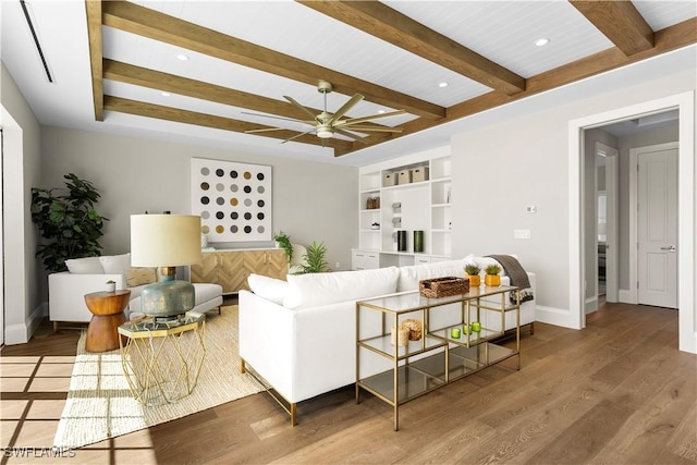 living area featuring ceiling fan, beamed ceiling, baseboards, and wood finished floors