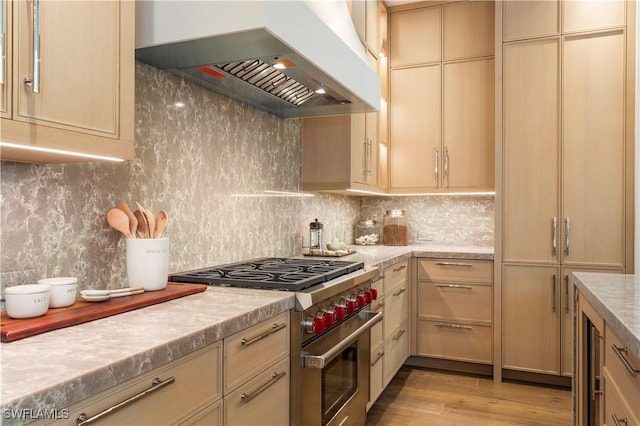 kitchen featuring backsplash, high end stove, light countertops, and wall chimney exhaust hood