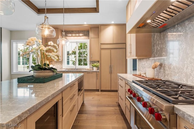 kitchen featuring light wood-type flooring, light brown cabinets, a tray ceiling, wall chimney exhaust hood, and built in appliances