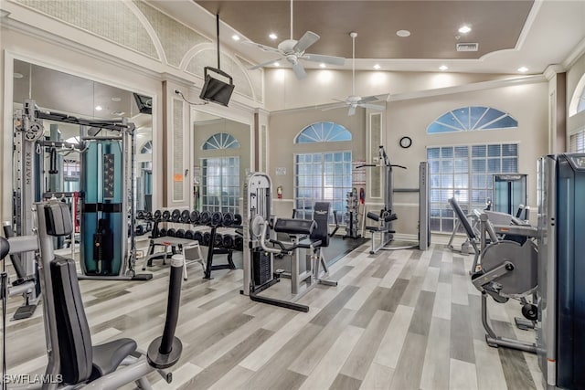 gym with light wood finished floors, visible vents, ornamental molding, ceiling fan, and high vaulted ceiling