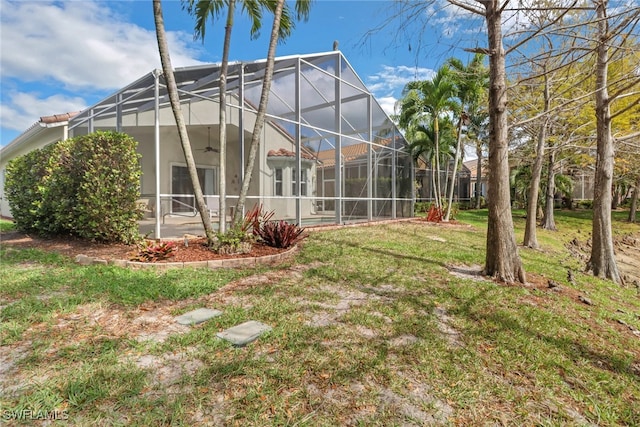 rear view of property featuring ceiling fan, a yard, glass enclosure, and stucco siding