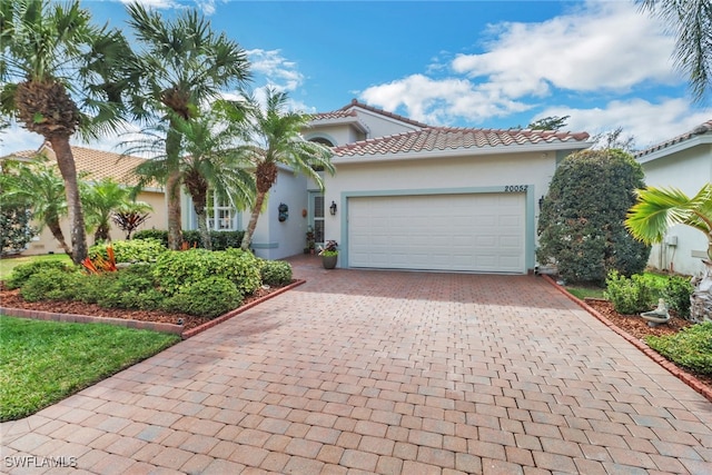 mediterranean / spanish-style house featuring decorative driveway, an attached garage, a tile roof, and stucco siding