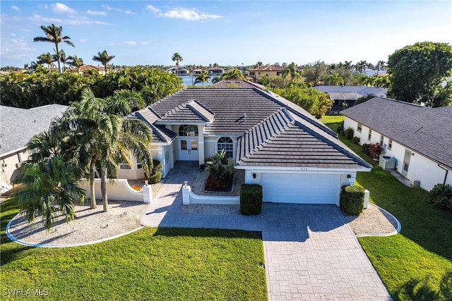 ranch-style house featuring an attached garage, a front lawn, decorative driveway, and a tiled roof