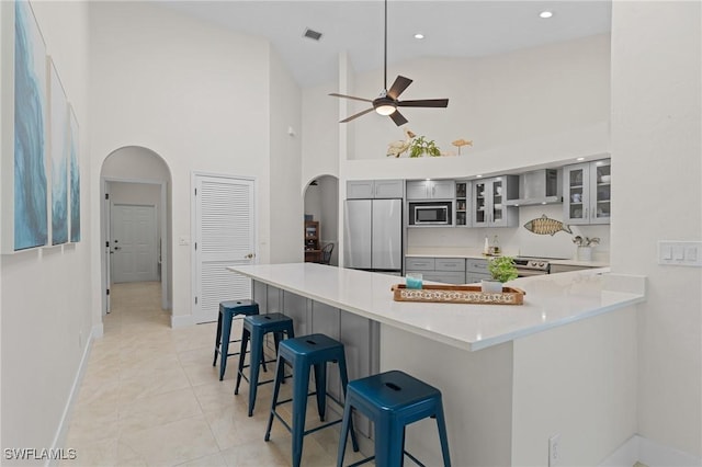 522 SW 51st Ter, Cape Coral, FL 33914 - kitchen featuring wall chimney range hood, a ceiling fan, gray cabinetry, high vaulted ceiling, and stainless steel appliances