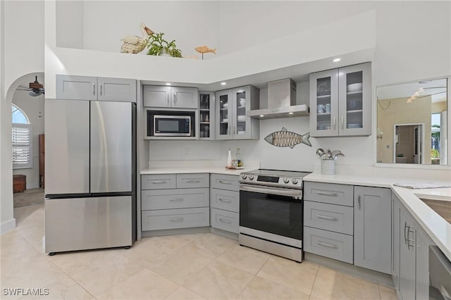 kitchen featuring arched walkways, wall chimney exhaust hood, glass insert cabinets, stainless steel appliances, and light countertops