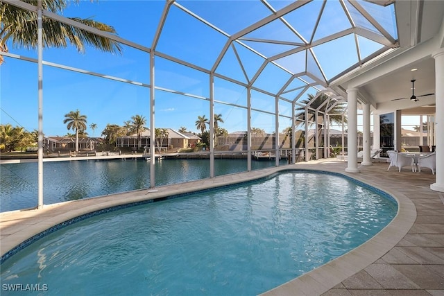 outdoor pool featuring a water view, glass enclosure, ceiling fan, and a patio