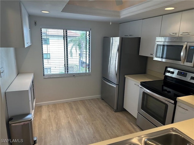 kitchen with appliances with stainless steel finishes, light hardwood / wood-style flooring, ceiling fan, a tray ceiling, and white cabinetry