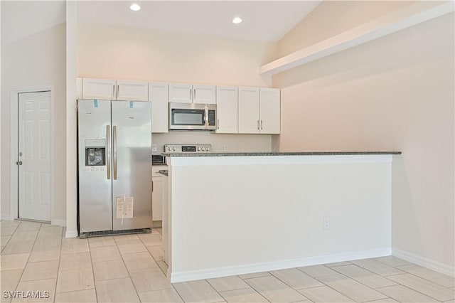 kitchen with appliances with stainless steel finishes, dark stone countertops, vaulted ceiling, and white cabinets