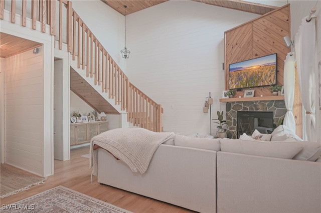 living room with light wood-type flooring, high vaulted ceiling, wood walls, and a stone fireplace