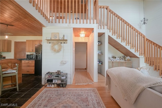 interior space with decorative light fixtures, black appliances, a high ceiling, light brown cabinets, and dark hardwood / wood-style floors