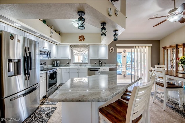 kitchen with stainless steel appliances, a kitchen island, a sink, white cabinetry, and a kitchen bar