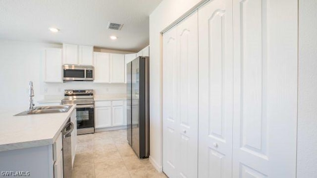 kitchen with appliances with stainless steel finishes, light tile patterned floors, sink, and white cabinetry