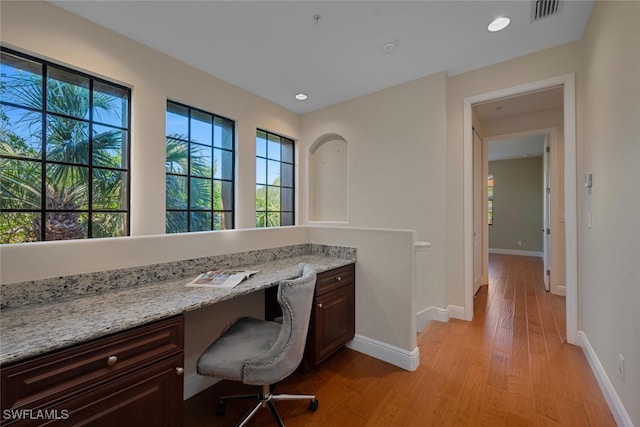 office area with light wood-style floors, baseboards, visible vents, and built in desk