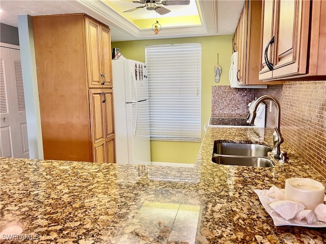 kitchen featuring sink, white appliances, tasteful backsplash, ceiling fan, and a raised ceiling