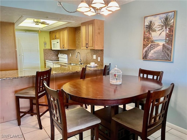 dining area featuring a raised ceiling, sink, light tile patterned flooring, and ceiling fan with notable chandelier