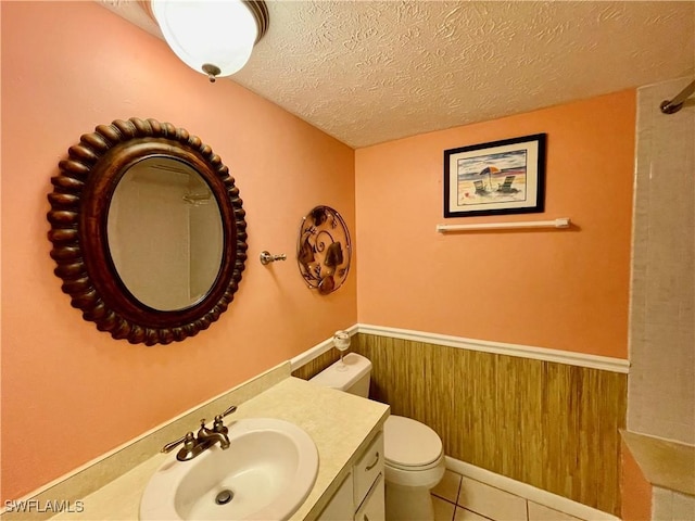 bathroom with vanity, a textured ceiling, toilet, tile patterned floors, and wooden walls