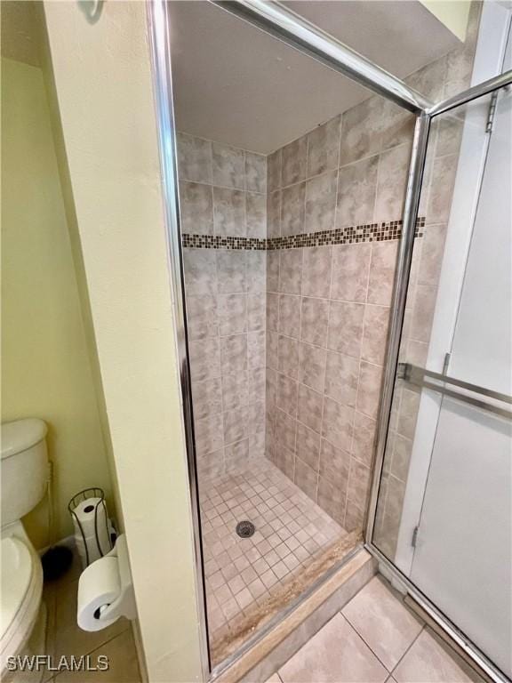 bathroom featuring toilet, tile patterned flooring, and a shower with shower door