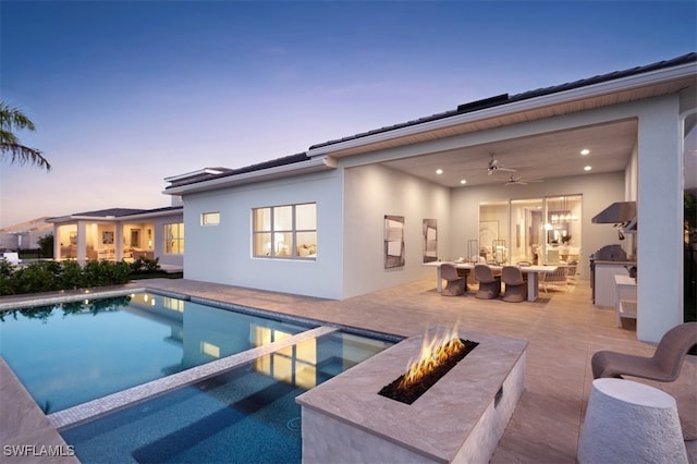 pool at dusk featuring a patio, an outdoor fire pit, and exterior kitchen