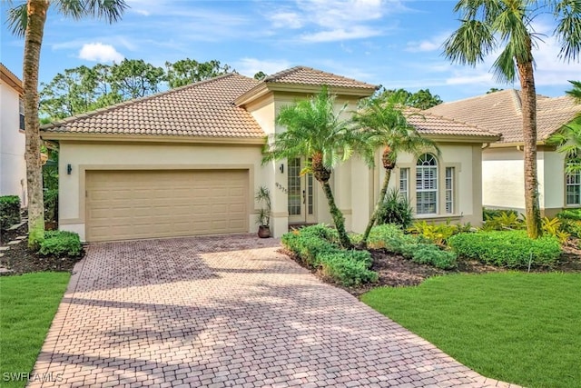 mediterranean / spanish house featuring decorative driveway, an attached garage, a tile roof, and stucco siding