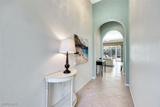 hall featuring light tile patterned floors, baseboards, and arched walkways