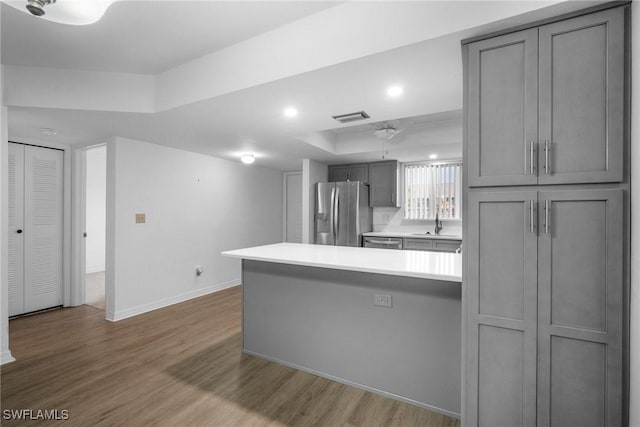 kitchen featuring hardwood / wood-style floors, appliances with stainless steel finishes, sink, gray cabinets, and a raised ceiling