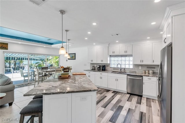 kitchen with hanging light fixtures, a kitchen island, sink, appliances with stainless steel finishes, and white cabinets