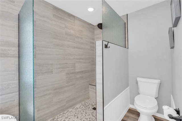 bathroom with wood-type flooring, a tile shower, and toilet