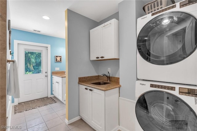 laundry area featuring light tile patterned floors, sink, cabinets, and stacked washer and clothes dryer