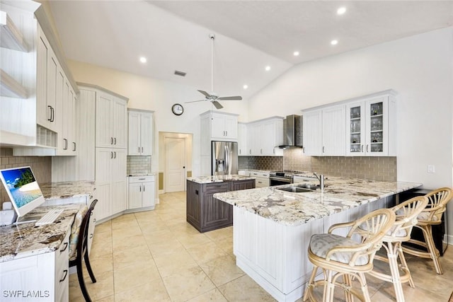 kitchen featuring wall chimney exhaust hood, appliances with stainless steel finishes, light stone counters, and a sink