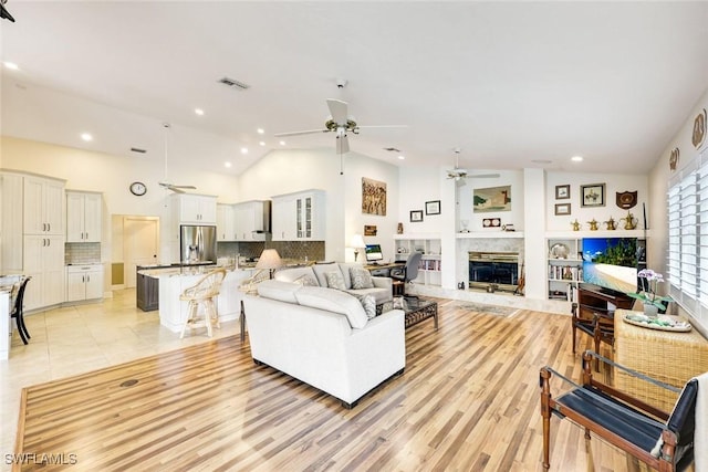 living area featuring visible vents, a ceiling fan, a premium fireplace, light wood-style floors, and high vaulted ceiling