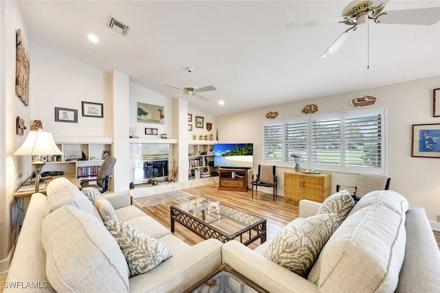 living area with wood finished floors, a ceiling fan, visible vents, vaulted ceiling, and a high end fireplace