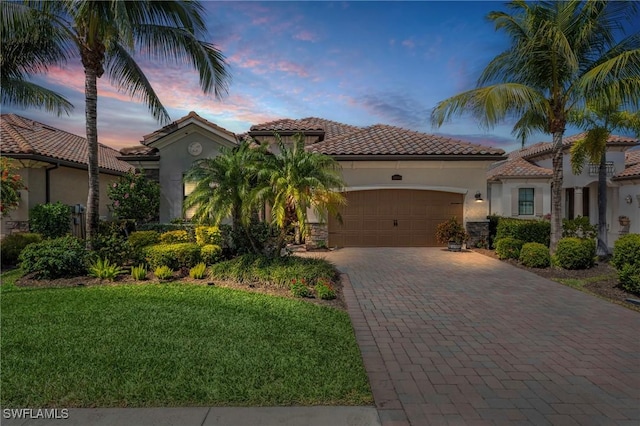 mediterranean / spanish-style home with stone siding, an attached garage, decorative driveway, a front lawn, and stucco siding