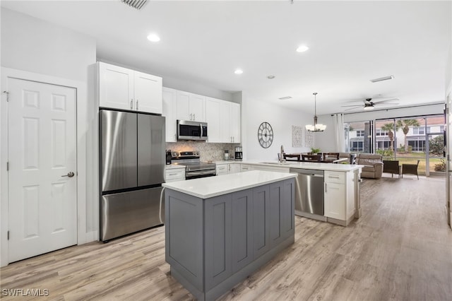 kitchen featuring kitchen peninsula, stainless steel appliances, decorative light fixtures, a kitchen island, and white cabinets