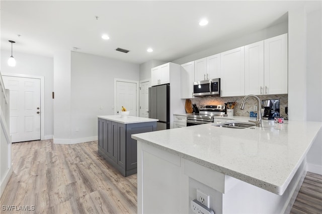 kitchen featuring white cabinetry, a center island, light stone counters, appliances with stainless steel finishes, and pendant lighting