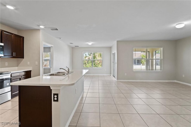 kitchen featuring light tile patterned floors, stainless steel appliances, a sink, light countertops, and an island with sink