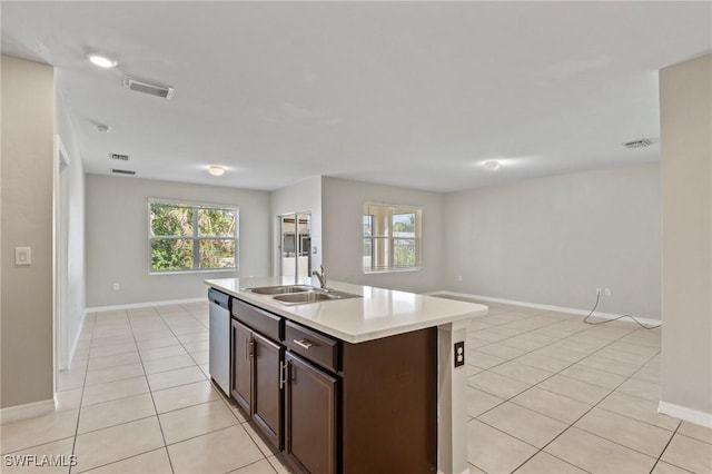 kitchen with light countertops, a kitchen island with sink, a sink, light tile patterned flooring, and dishwasher