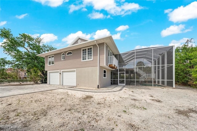 back of house featuring glass enclosure, an attached garage, driveway, and stucco siding