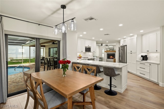 dining space with recessed lighting, visible vents, a ceiling fan, light wood-type flooring, and a warm lit fireplace