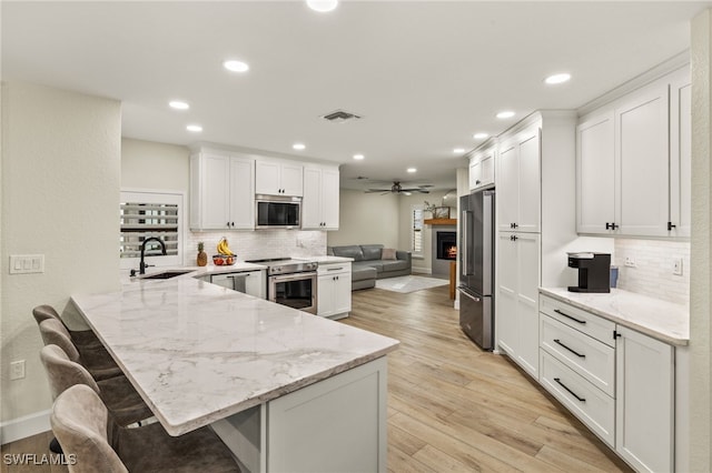 kitchen featuring light stone counters, visible vents, appliances with stainless steel finishes, a sink, and a peninsula