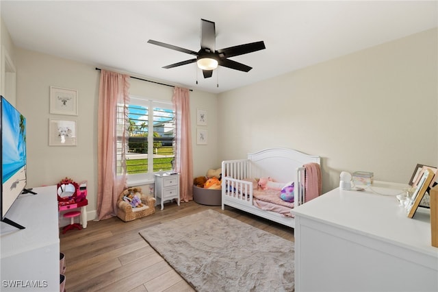 bedroom featuring ceiling fan, a crib, and light wood-type flooring